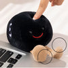 A hand is holding a black, fuzzy plush doll shaped like an apple next to a laptop keyboard.