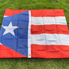 A large, red and blue Puerto Rico national flag banner displayed outdoors on green grass.