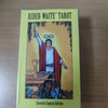 A yellow deck of Rider-Waite Tarot cards with a Spanish English Edition guidebook displayed on a wooden surface.