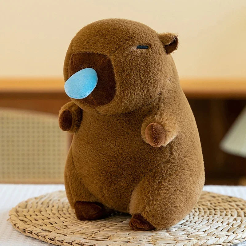 A brown capybara plush toy with light blue eyes sitting on a woven mat.