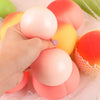 A hand is holding a pink peach-shaped squeeze toy with various colored balls on a sheer fabric background.