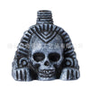 A dark gray skull with intricate patterns and facial features, resembling an Aztec death whistle or screaming noise maker.