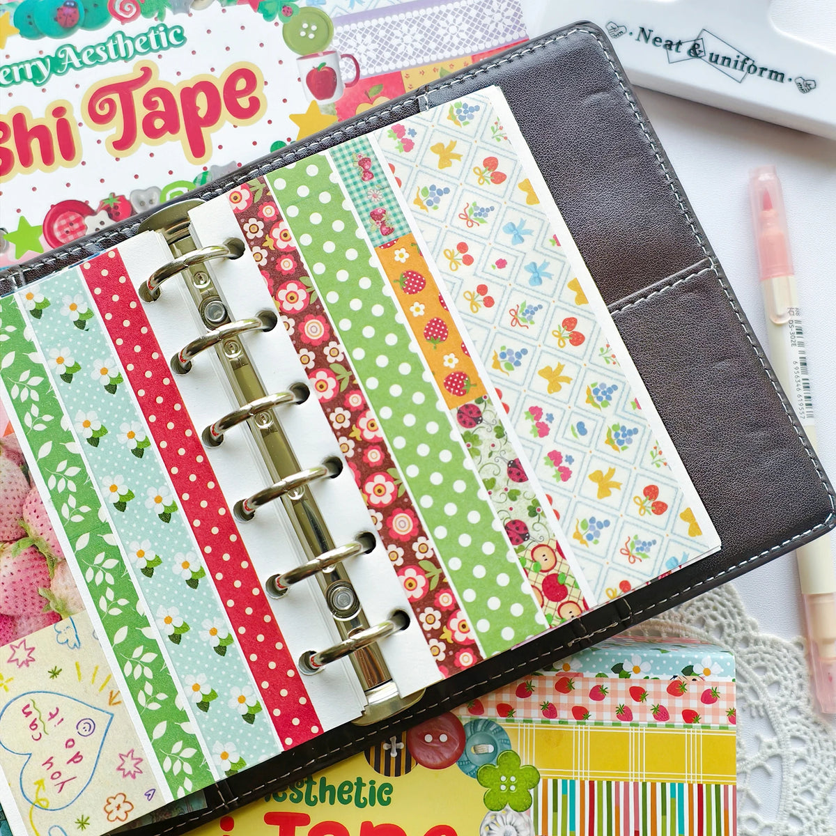 A close-up of a craft tape set featuring various patterned washi tapes in red, green, and white on a dark gray folder.