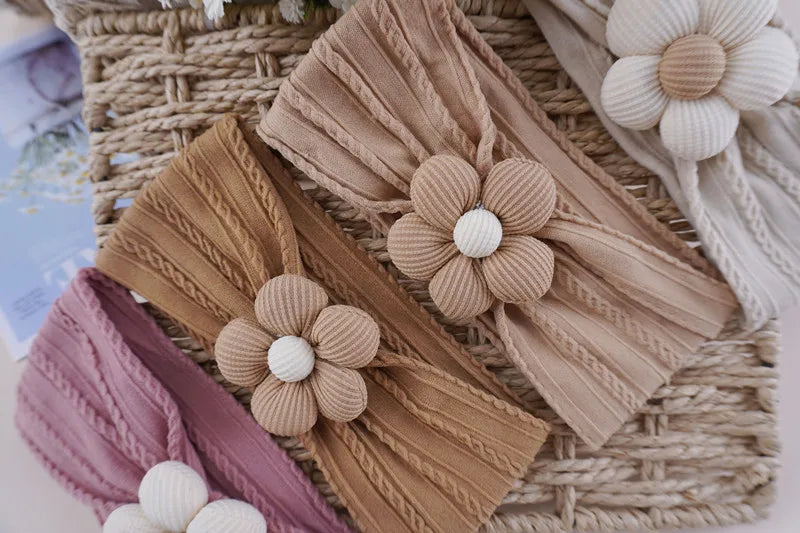 A collection of floral elastic baby headbands in beige, pink, and cream resting on a woven mat.