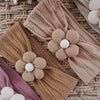 A collection of floral elastic baby headbands in beige, pink, and cream resting on a woven mat.