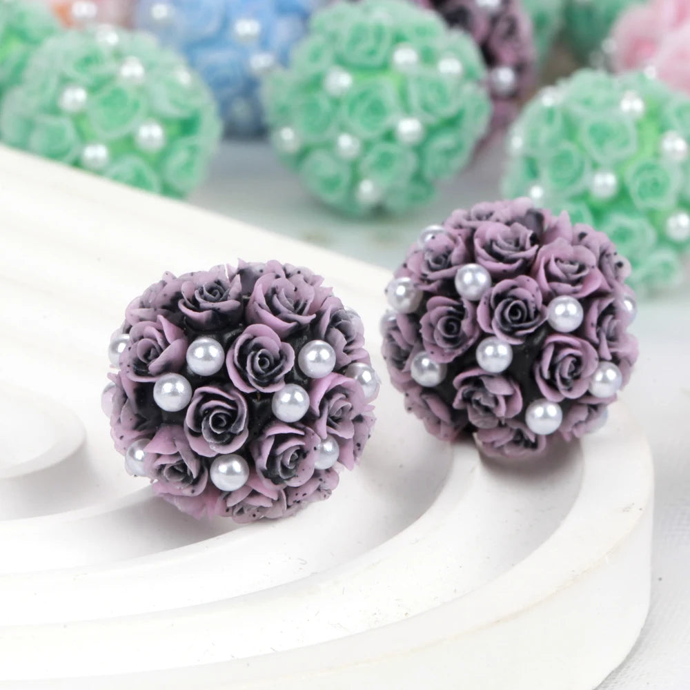 A close-up of purple rose flower ball acrylic beads for jewelry making resting on a white surface.