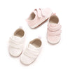 A set of classic white soft-sole baby first walkers with pink accents shown from above.