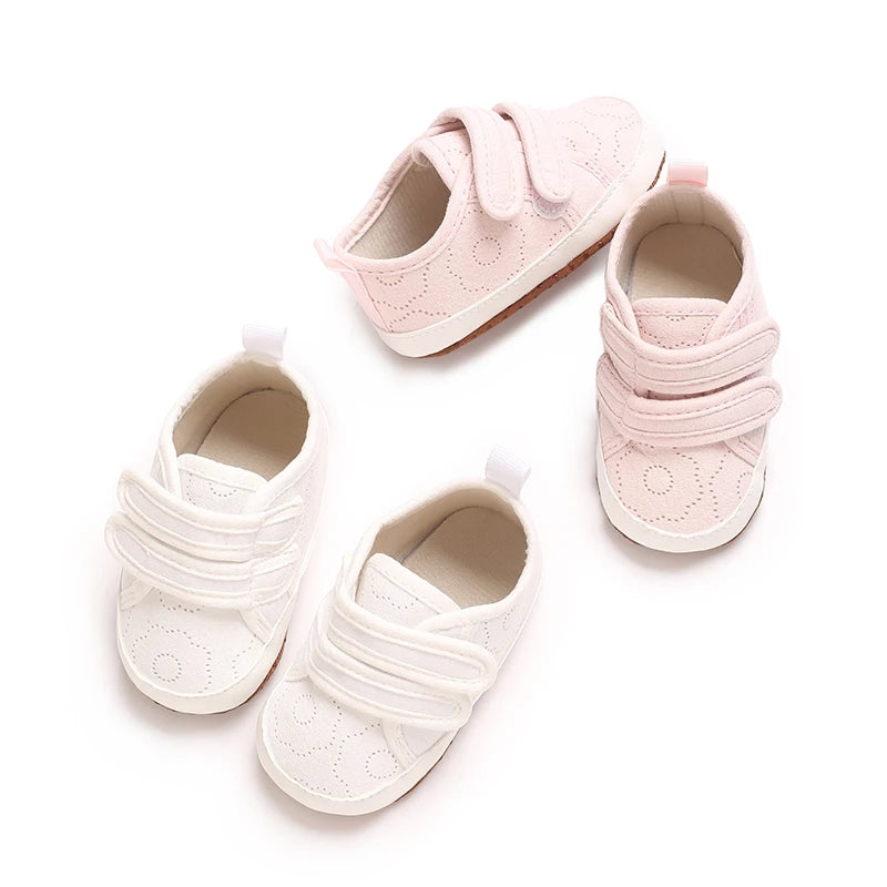 A set of classic white soft-sole baby first walkers with pink accents shown from above.
