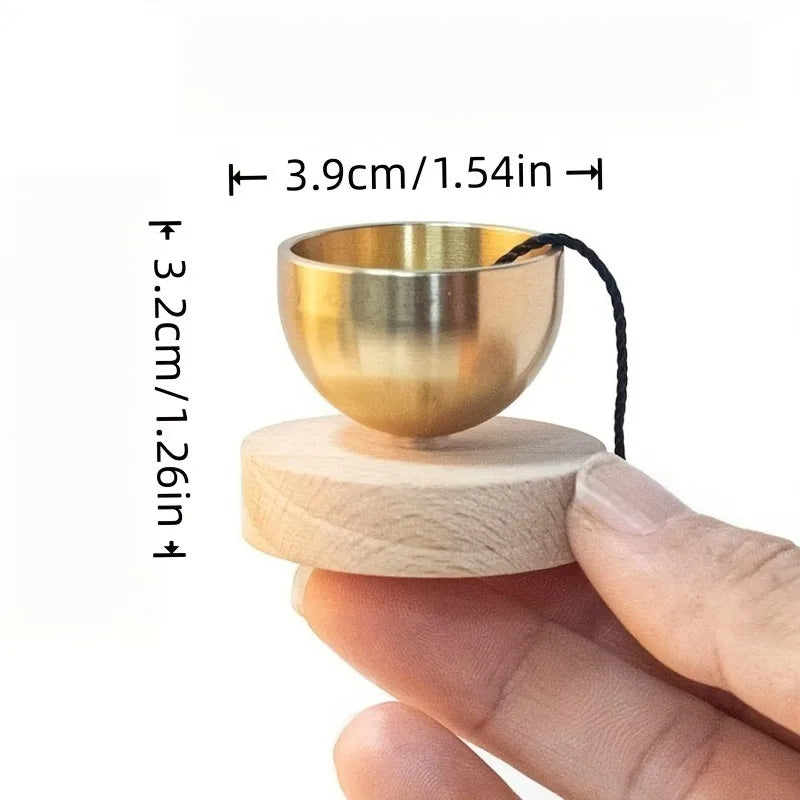 A small brass singing bowl resting on a wooden base, shown being held by a hand.
