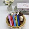 A set of ergonomic crochet hooks, stitch markers, and needles in various colors stored in a natural fiber basket.