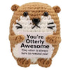 A handmade crochet owl toy with brown fur and white facial markings, featuring a sign that reads You're Otterly Awesome.
