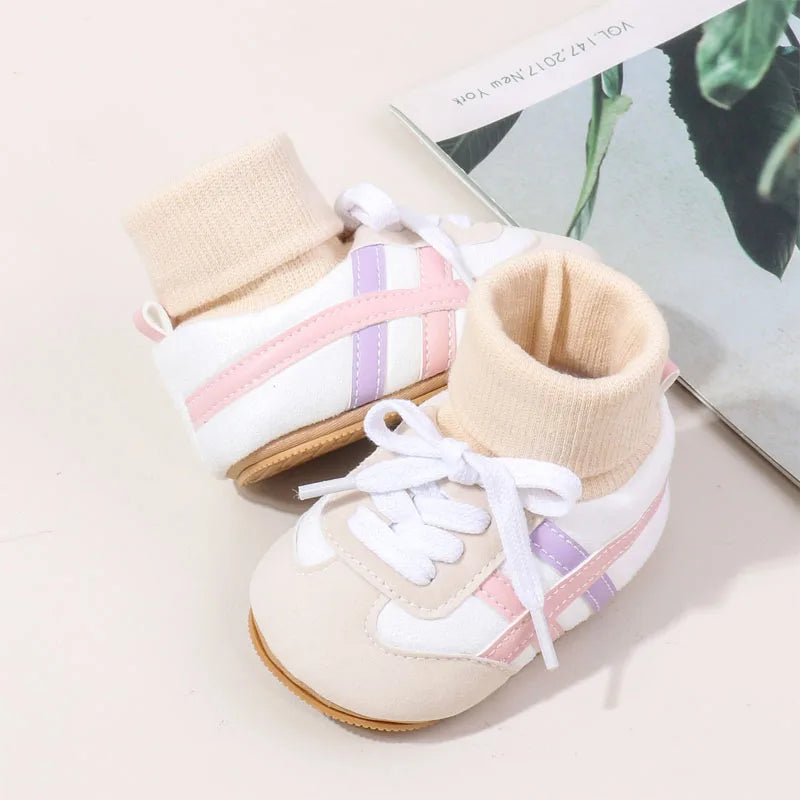 A pair of light beige baby booties with white and pink stripes and anti-slip soles resting on a book.