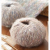 A ball of soft gray alpaca blend yarn resting on a wooden surface next to knitting needles.