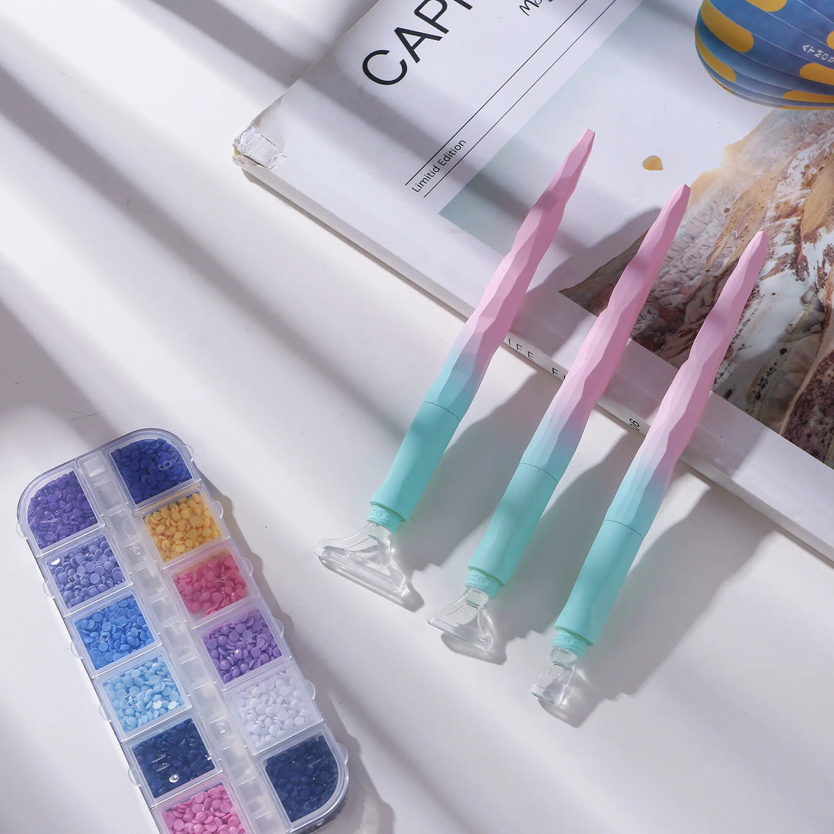 A set of diamond painting pens in pink and teal colors displayed next to a plastic storage case.