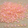 A pile of translucent pink and orange tulip flower glass beads scattered on a beige fabric surface.
