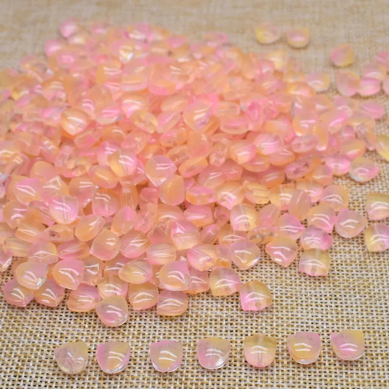 A pile of translucent pink and orange tulip flower glass beads scattered on a beige fabric surface.