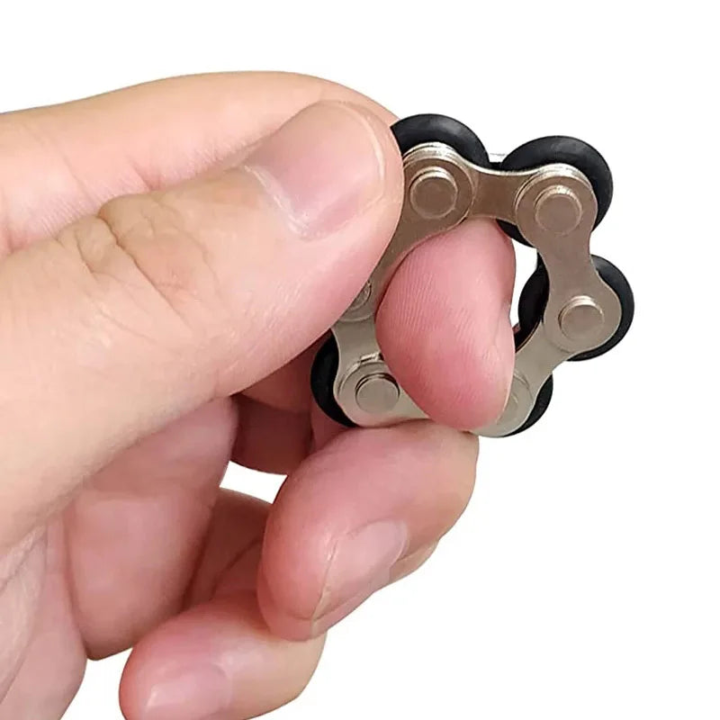 A hand holds a silver metal fidget toy with black rubber rollers, resembling a bike roller chain.