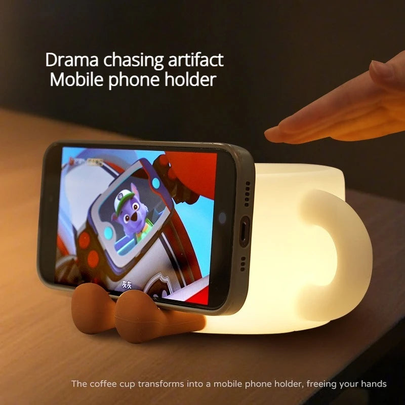 A mobile phone holder made from a coffee cup shaped night light, illuminating the device.