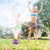 A young girl sprays water with an octopus-themed sprinkler in a grassy outdoor setting.
