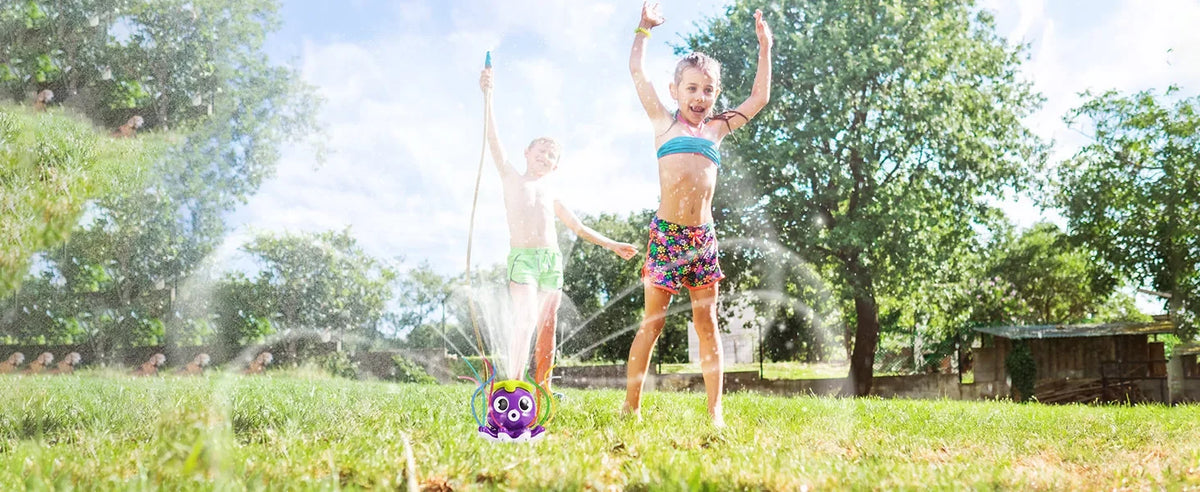 A young girl sprays water with an octopus-themed sprinkler in a grassy outdoor setting.