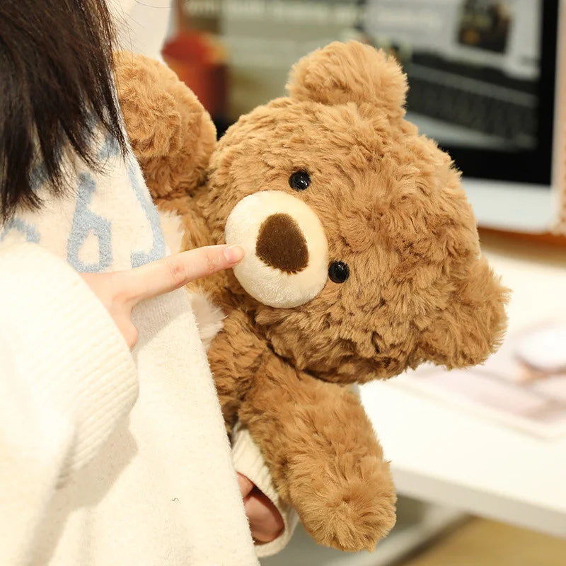 A person's finger is pointing at the face of a brown teddy bear plush toy.