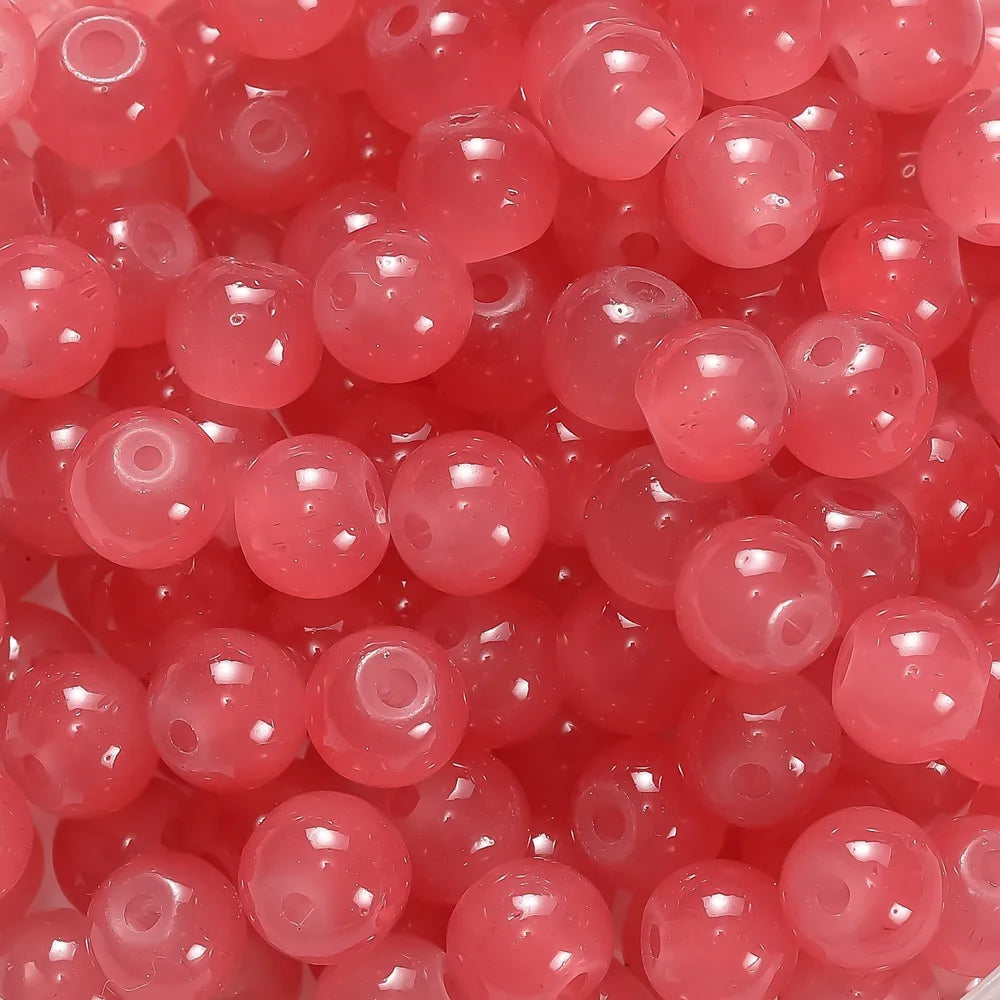 A close-up view of small, round, translucent pink glass beads for DIY jewelry making.