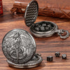A silver steampunk dragon pocket watch dice case with seven mini dice resting on a wooden surface.