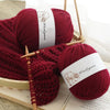 A close-up of a deep red yarn skein used for knitting, displayed on a wooden surface.