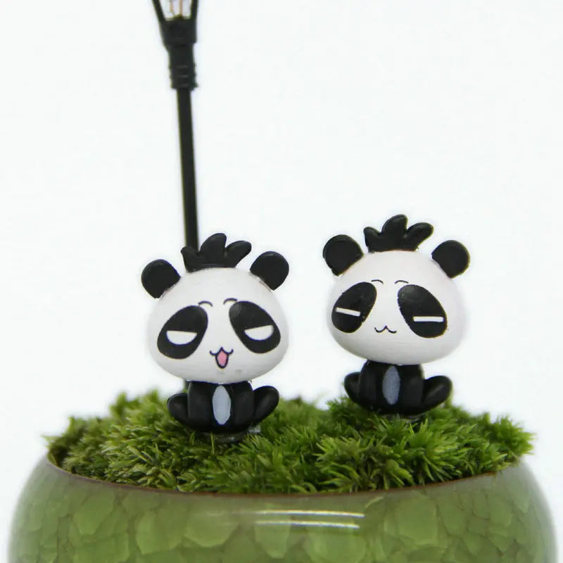 A pair of black and white panda miniature animal figurines displayed on a mossy green surface.