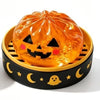 An orange pumpkin shaped squishy fidget toy with a carved face is placed in a black slotted container.