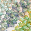 Green and blue maple leaf glass beads scattered on a light background for DIY jewelry making