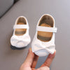 A hand holds a white lace-trimmed baby girl moccasin shoe with a bow, showing the interior and exterior detail.