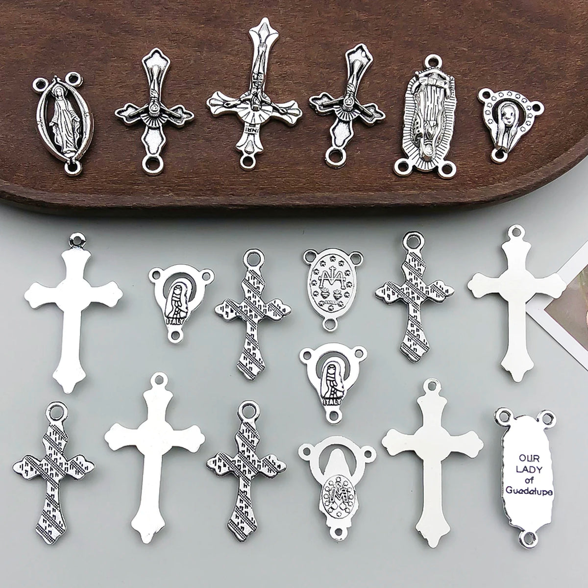 A collection of vintage antique silver cross charms and pendants for jewelry making displayed on a dark wooden surface.