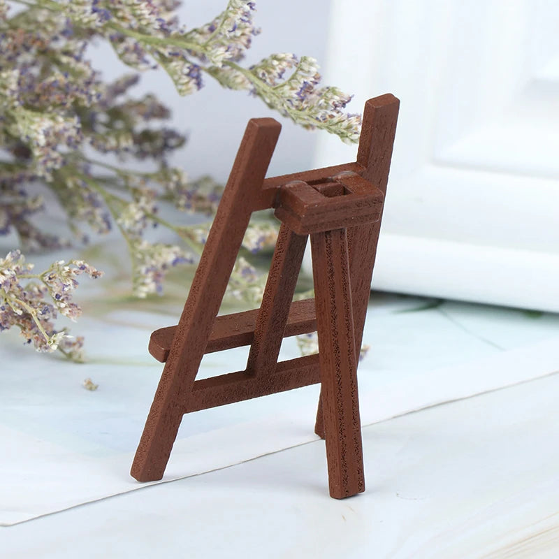 A small wooden artist easel used for dollhouses, made of brown wood, set against a light background with lavender branches.