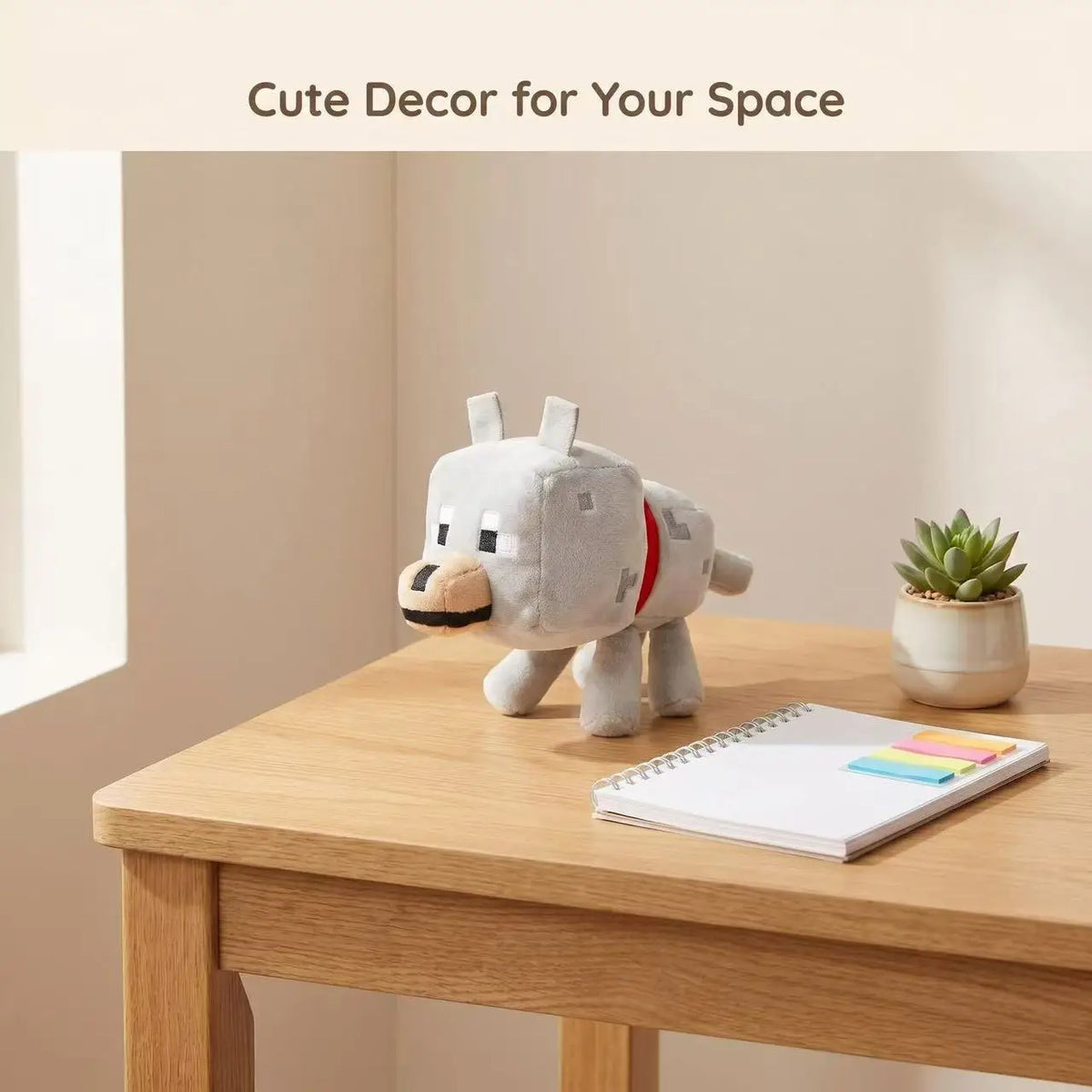 A cute gray wolf plush toy sitting on a wooden table next to a notebook and a potted succulent plant.