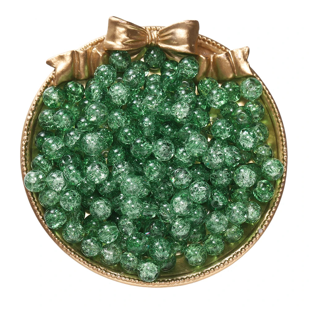 A pile of green glass crackle beads for jewelry making displayed in a gold-toned dish with a bow.