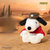 A white dog plush doll dressed as a western cowboy with a brown hat and red bandana sitting in a desert landscape.