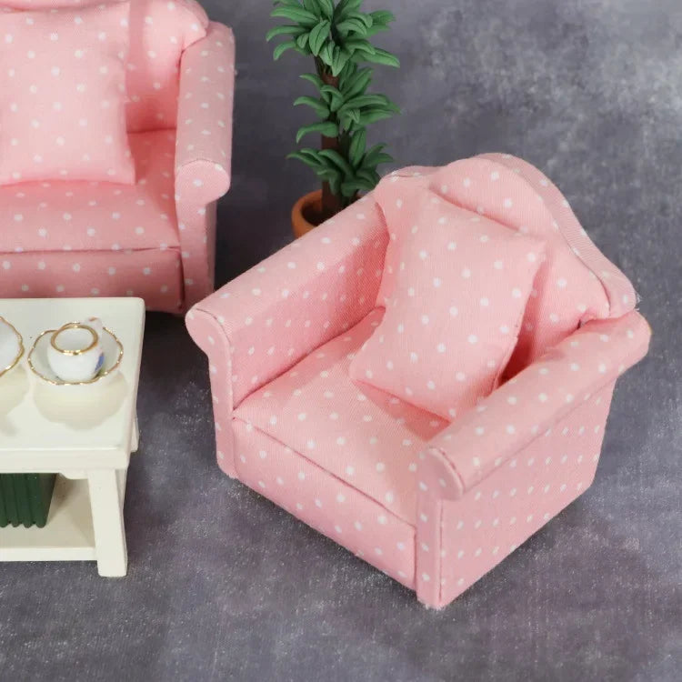 A pink 1:12 scale mini sofa and pillow set with white polka dots placed on a gray surface.