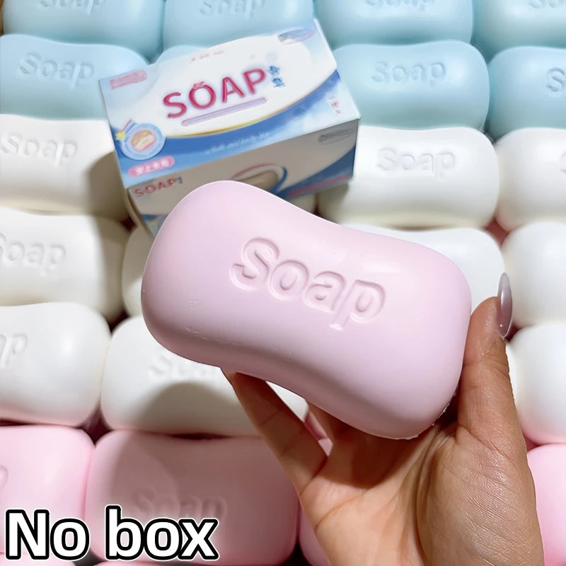 A hand holds a pink soap ball squishy fidget toy surrounded by other white and pink soap products.
