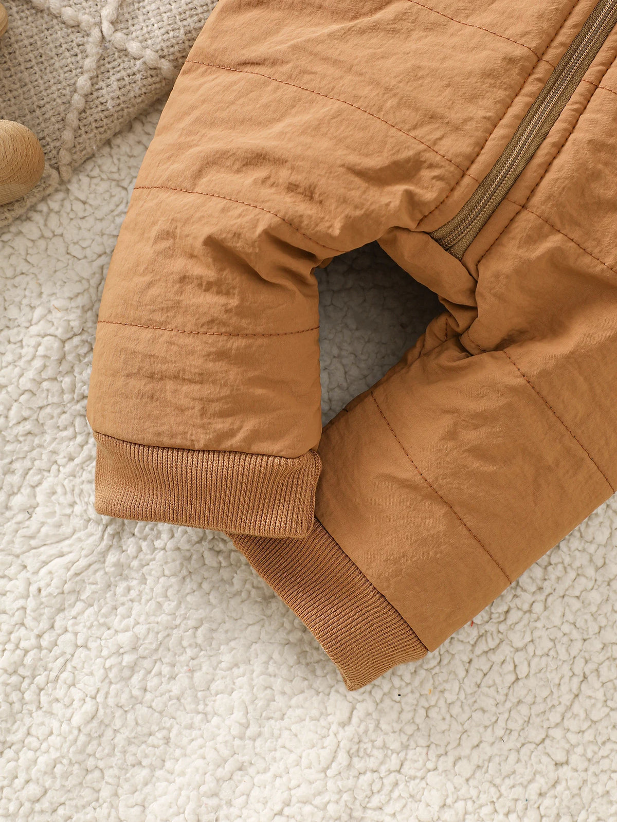 A close-up of a tan fleece romper for infants lying on a white, fluffy surface.