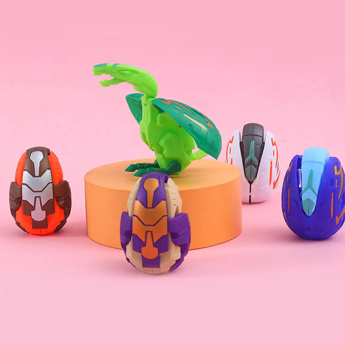 A green dinosaur egg toy is displayed next to a purple and orange dinosaur egg toy on a pink background.