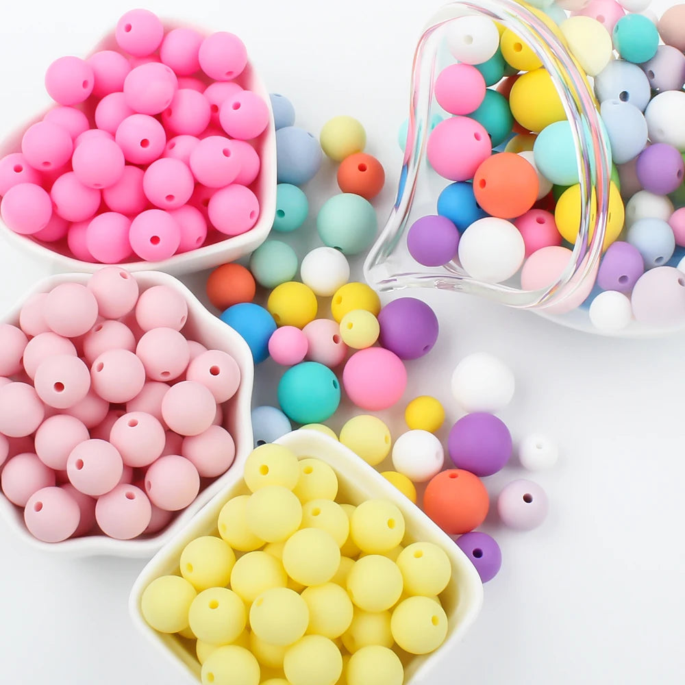 A collection of colorful round silicone beads in various shades of pink, yellow, blue, and purple are displayed in small bowl