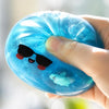 A hand holds a blue glitter squishy toy shaped like a shark with sunglasses and a small fish inside.