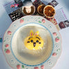 A yellow Hachiware Usagi squishy stress relief toy is placed in a clear plastic bag on a decorative plate surrounded by small