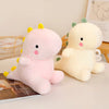 A pink dinosaur plush toy with yellow horns and a cream-colored dinosaur plush toy sitting on a white surface.