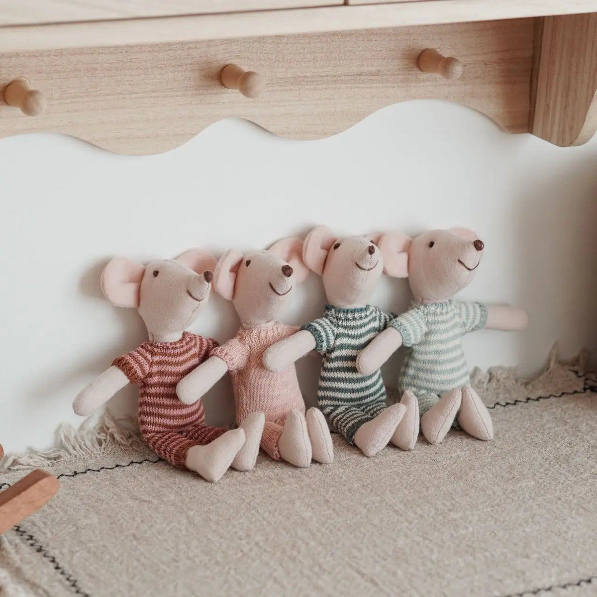 A row of four handmade mouse plush dolls with retro striped outfits sitting on a light fabric surface.