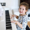 A young girl is playing a piano keyboard with note stickers on the white and black keys.