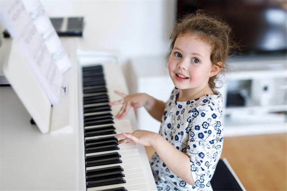 A young girl is playing a piano keyboard with note stickers on the white and black keys.