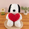 A white plush toy resembling Snoopy with black ears and a red heart attached, sitting on a woven mat.