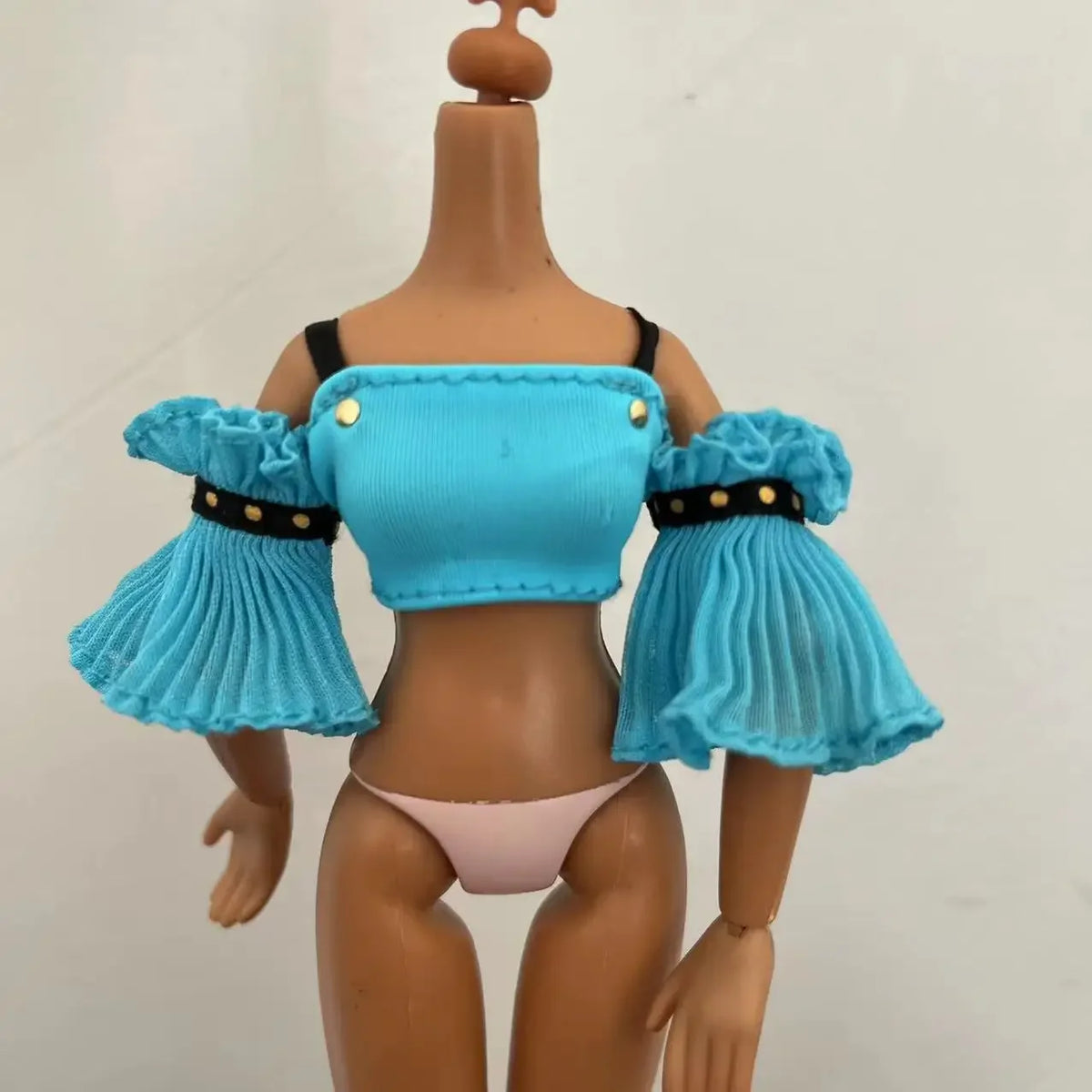 A brown doll with a light blue top and ruffled sleeves, wearing pink underwear.